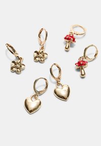 Orecchini a goccia color oro con ciondoli: un fiore, un cuore e un fungo rosso, con superfici lucide e chiusura a cerchio.