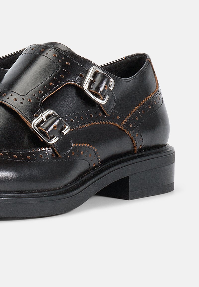 Scarpe in pelle nera con punta arrotondata, caratterizzate da un design decorativo perforato, due fibbie metalliche e un tacco basso a blocco.