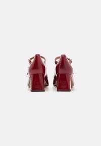 Red patent leather heels with a block heel design and adjustable ankle strap. Smooth texture and rounded toe.