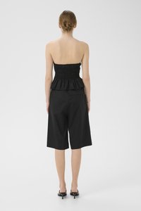Svart peplum topp med smock-design, kombinert med kne-lange svarte shorts. Glatt stoffoverflate og strukturert silhuett. Svart åpen tå hæler.