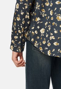 Camicia a bottoni floreale con sfondo blu navy e fiori crema e senape, rifinita con un orlo curvo e polsini abbottonati.