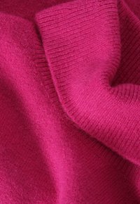 Dzianina w kolorze fuksji o gładkiej fakturze, z prążkowaniami i miękkimi, subtelnymi odcieniami koloru w całej powierzchni.