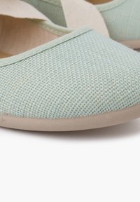 Chaussure slip-on en toile bleu clair avec une finition texturée, bout rond et semelle en caoutchouc beige. Design simple, sans embellissements supplémentaires.