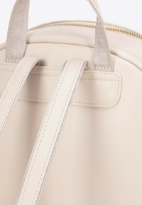 Beżowy plecak skórzany z podwójnymi paskami o miękkiej fakturze i kontrastującym szyciu, prezentujący minimalistyczny design i zamek błyskawiczny u góry.
