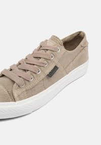Beige Canvas Sneaker mit beigen Schnürsenkeln, weißer Gummisohle, strukturiertem Stoff und einem schwarzen Logopatch an der Seite. Abgerundetes Design der Zehenpartie.