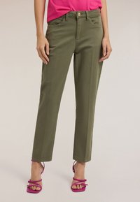 Oliwkowe spodnie o prostym kroju, z kieszeniami z przodu i zapięciem na guzik. W zestawieniu z różowymi sandałkami na obcasie dla kontrastu.