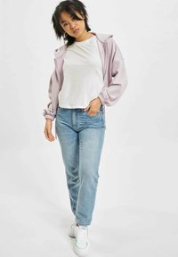 Lys lilla overdimensjonert hettegenser, kombinert med en hvit t-skjorte og blå jeans. Fottøyet inkluderer hvite joggesko med grønne detaljer.