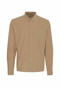 Camisa de manga larga y cuello en tejido beige claro. Presenta un cierre de botones en la parte delantera y un solo bolsillo en el pecho. Textura suave con un diseño limpio.