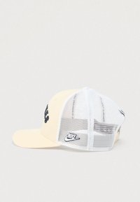 Gorra camionera de rejilla Nike en beige y blanco con logo bordado en negro en la parte frontal y parche del swoosh de Nike en el panel lateral de malla blanca.
