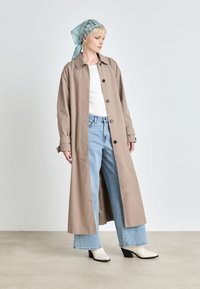 Długi beżowy płaszcz z czarnymi guzikami, noszony na białej bluzce i jasnoniebieskich szerokich dżinsach. Dopełniony białymi botkami na obcasie i wzorzystym szalikiem.