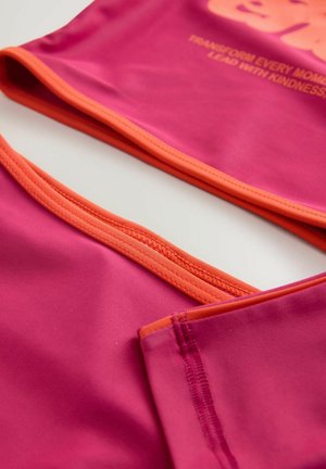 Fuchsiový sportovní top s oranžovými lemy a prošitím. Má hladký povrch a grafický slogan v světle růžovém odstínu.
