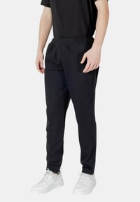 Schwarze Sweatpants mit lockerer Passform, Kordelzugbund und Seitentaschen, kombiniert mit weißen Sneakers für den Kontrast. Glatte Textur.