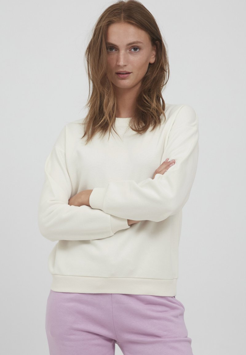 Krämfärgad sweatshirt med lång ärm, ribbade mudd och nederkant. Mjuk textur, avslappnad passform, tillsammans med lavendelfärgade sweatpants.