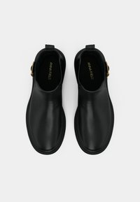 Black leather ankle boots with a rounded toe, flat sole, side gold buckle hardware, and subtle brand logo embossed inside.