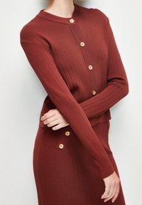 Bordowy prążkowany kardigan z długimi rękawami i okrągłym dekoltem, ozdobiony złotymi guzikami z przodu i na dole.