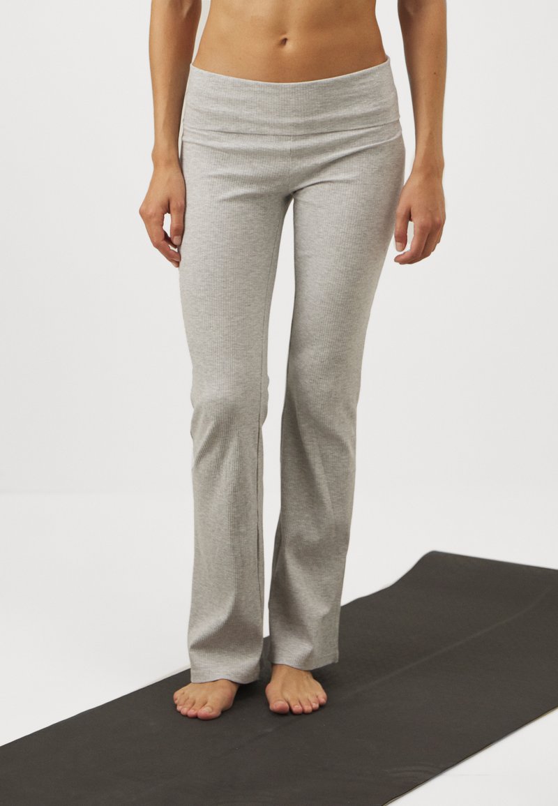 Grå, ribbede yogabukser med bred midje, flagrende design og myk tekstur, vist på en svart yogamatte.