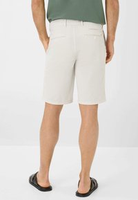 Pantaloni corti beige chiaro realizzati in un tessuto morbido, con taglio dritto e tasche posteriori discrete. Abbinati a sandali neri.