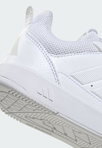 Zapato deportivo blanco con parte superior texturizada y detalles de malla, suela lisa y logotipo de tres rayas en el lateral.