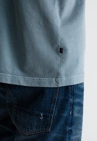 Lichtblauwe katoenen t-shirt met een rechte zoom, voorzien van een klein zwart logo label. Draag het met donkerblauwe jeans met een witte logo stiksel.