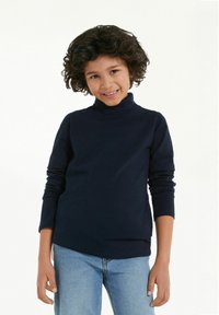 Dunkelblauer Rollkragenpullover aus weichem, dehnbarem Material, mit langen Ärmeln und körpernahem Schnitt, kombiniert mit hellblauen Jeans.