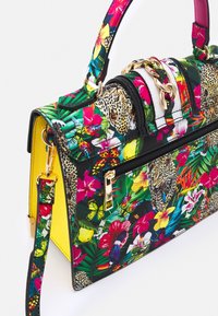 Sac à main avec imprimé floral tropical coloré, papillon et léopard, détail chaîne dorée, fermeture éclair noire et panneau latéral jaune texturé.