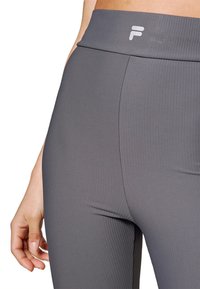 Leggings cinza canelados com uma cintura alta e um detalhe de logo branco. O tecido parece texturizado e elástico, proporcionando conforto durante o uso.