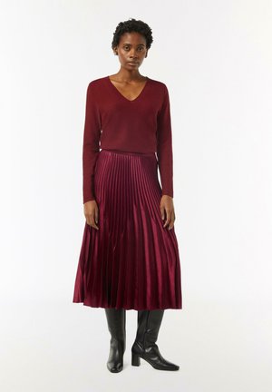 Burgundy long-sleeve V-neck top paired with a pleated maxi skirt in a rich burgundy hue, complemented by black knee-high boots.