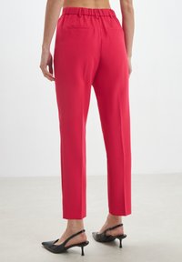 Rote, taillierte Hosen mit einem elastischen Bund. Verfügt über zwei Gesäßtaschen, eine glatte Textur und ein mittelhohes Design, kombiniert mit schwarzen High Heels.