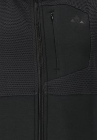 Veste de sport noire avec fermeture éclair sur le devant, dotée d'un tissu en mesh texturé aux épaules et d'une petite poche sur la poitrine gauche.
