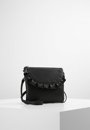 Sac bandoulière en cuir noir avec détail de rabat froncé, forme rectangulaire et sangle réglable, posé sur une surface blanche sur un fond uni.