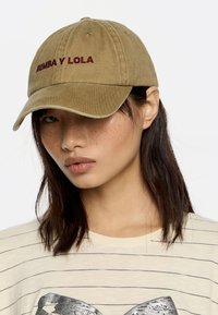 Khaki baseballhattu, jossa on brodeerattu tummanpunainen "BIMBA Y LOLA" -teksti. Pehmeä kangas, kaareva lippa, kuusi tuuletusaukkoa ja rento muotoilu.
