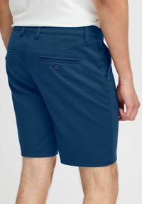 Marineblå shorts laget av lett stoff, med to baklommer med knappelukking og en skreddersydd passform, synlig søm.