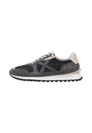Zapatilla baja gris y negra con suela blanca, cierre de cordones, paneles de ante y tela, y detalle beige en el talón.