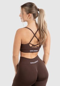 Conjunto de ropa de deporte marrón que incluye un sujetador deportivo con tirantes cruzados en la espalda y leggings de cintura alta, ambos con detalles del logotipo.