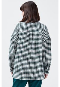 Oversized shirt met lange mouwen en geknoopte manchetten, zwart-wit houndstooth-patroon, met een plooi aan de achterkant.
