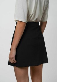 Sort miniskirt med en struktureret pasform, der har en glat tekstur og en høj talje, parret med en lysefarvet, løstsiddende skjorte.