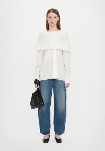 Witte blouse met een oversized kraag, knoopsluiting en gecombineerd met blauwe wijde jeans. Een zwarte handtas en elegante zwarte ballerina's maken de look compleet.