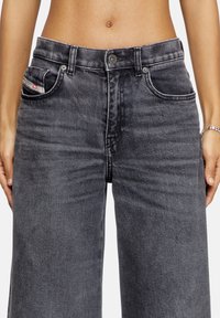 Jeans en denim gris taille haute avec jambes larges, dotés de poches avant, d'une texture délavée et d'une fermeture à bouton en argent. Détail de marque subtil sur la poche.