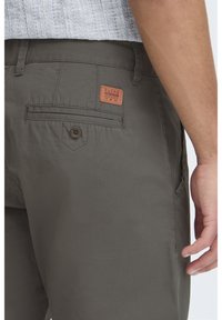 Olive green cargo shorts featuring a leather brand patch, flap pocket with button detail, and a soft, lightweight fabric texture.