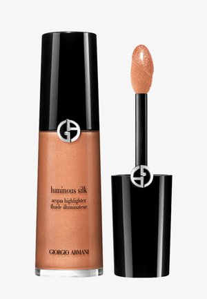 Luminous Silk liquido illuminante di Giorgio Armani in una bottiglia di vetro trasparente con un tappo nero. Presenta un applicatore conico e una tonalità bronzea scintillante.