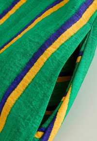 Gros plan d'un tissu vert avec des rayures jaunes et violettes et une ouverture visible de la poche latérale de couture.