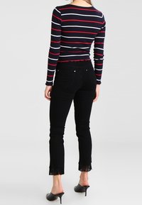 Randig långärmad tröja i marinblått, rött och vitt, ihop med svarta högmidjade jeans med fransar i fållarna och en slät yta.