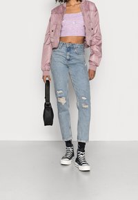 Skórzana różowa kurtka bomberka na dopasowanym, fioletowym crop topie z prążków, połączona z nadszarpanymi jasnoniebieskimi dżinsami i czarnymi trampkami wysokimi. Czarna torba.