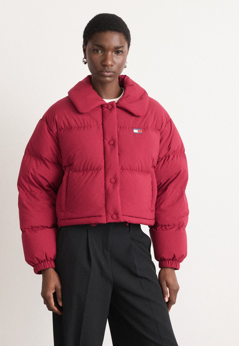 Κόκκινο κοντό μπουφάν με μεγάλο γιακά, κουμπιά με κλιπ και εμπρός τσέπες; φέρει ένα μικρό λογότυπο στο αριστερό στήθος.