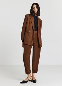 Blazer doppiopetto in corduroy marrone abbinato a pantaloni a sigaretta coordinati. Top costa nera e décolleté slingback neri con dettagli.