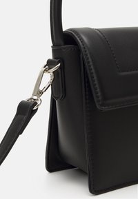 Sac à main en simili cuir noir avec une forme structurée, doté d'un fermoir en métal argenté, de bords surpiqués et d'une bandoulière pour un port polyvalent.