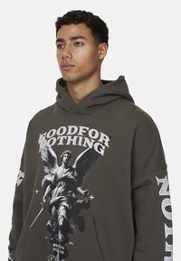 Sweat à capuche vert foncé avec un graphisme sur le devant représentant une statue et un texte en gras. Tissu doux, poche kangourou et accents blancs sur les manches.