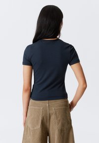 T-shirt ajusté bleu marine à manches courtes, texture lisse. Porté avec un pantalon en velours côtelé marron clair à jambes larges avec des poches arrière.