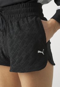 Juodi šortai su tekstūruotu raštu, elastinga juosmens juosta ir šoniniais kišenėmis. Apatinėje dalyje yra mažas baltas Puma logotipas.