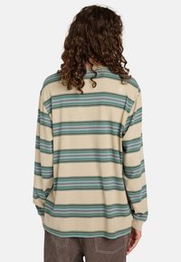 Camicia a maniche lunghe beige con strisce orizzontali blu, verdi e rosse; vestibilità rilassata e tessuto di cotone morbido. Nessun hardware o accentuazione notevole.